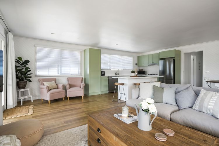 A snug living space featuring two blush chairs, a cushioned seat, sofa, coffee table, television, and scenic vistas of mountains and the veranda peeking through the windows.