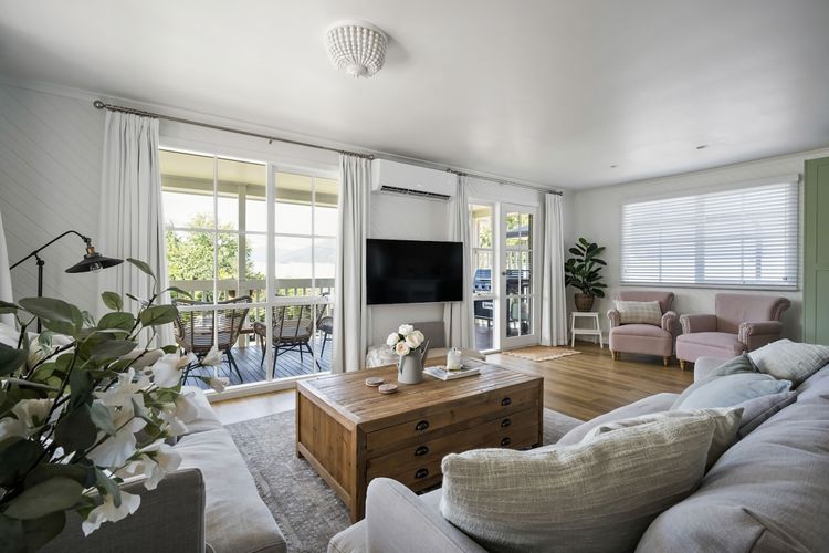 A snug living space featuring two blush chairs, a cushioned seat, sofas, coffee table, television, reverse cycle, and scenic vistas of mountains and the veranda peeking through the windows.