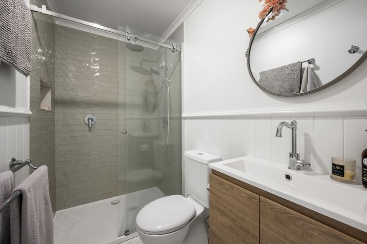 A refurbished bathroom showcasing a shower, toilet, spacious basin, towel rack, mirror, and storage beneath the basin.