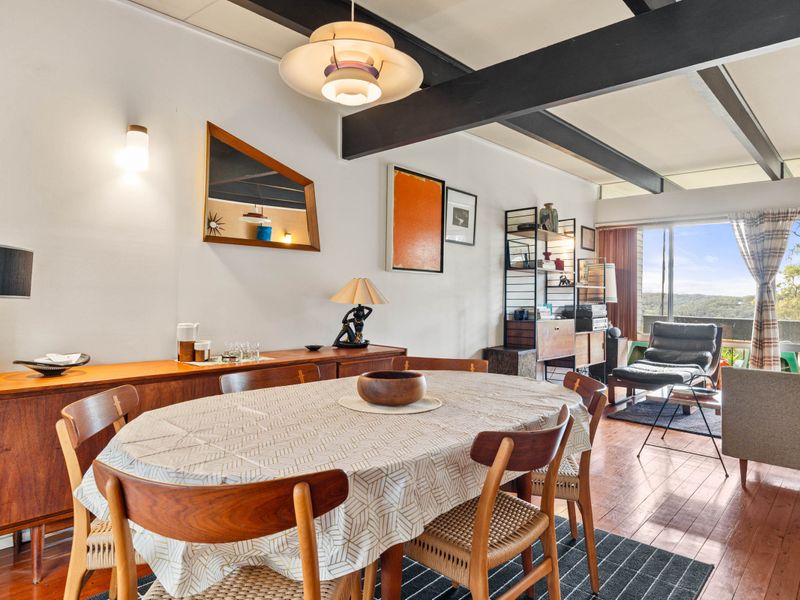 Dining room with mid-century modern furniture, including an oval table covered with a tablecloth, wooden chairs, a sideboard, and a unique pendant light. 
