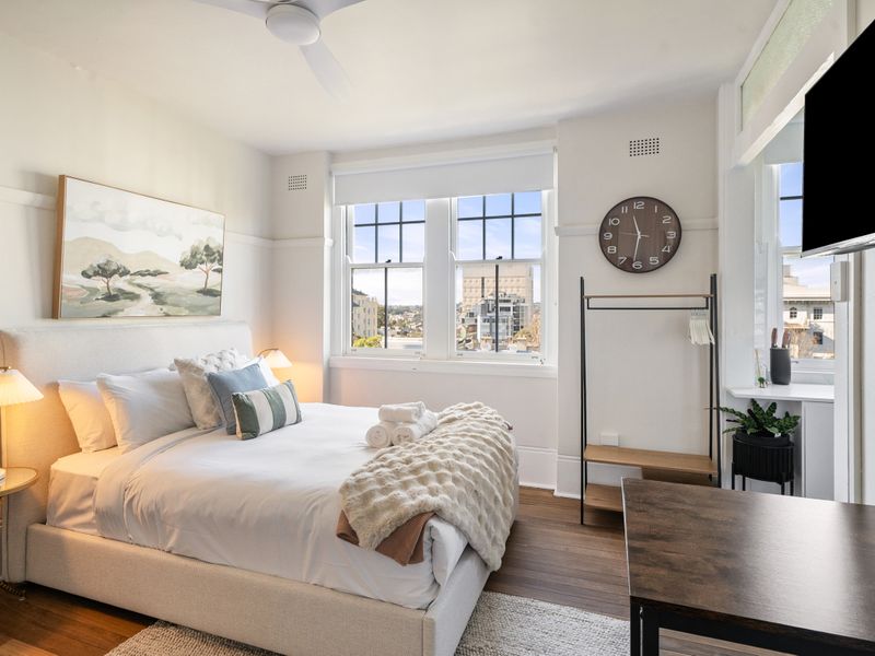 A bright and inviting bedroom featuring a comfortable bed with crisp white linens, a plush throw blanket, and decorative pillows. 